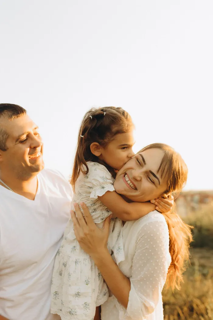 A mother and father laughing outdoors with their young daughter
